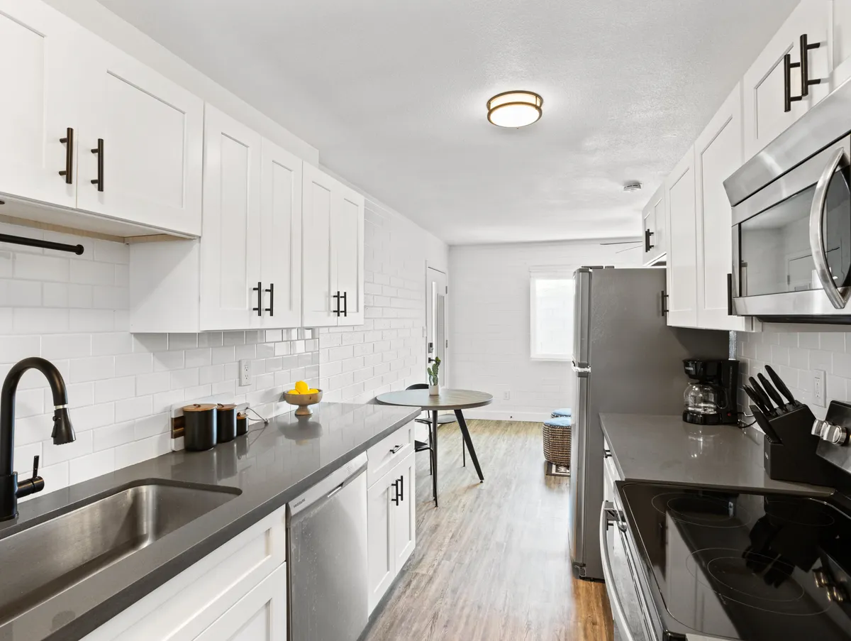 A bright kitchen with a central island, stainless steel appliances, white cabinetry, and natural light streaming in through the window. The space feels functional and welcoming, ideal for cooking, casual dining, and socializing around the kitchen island.