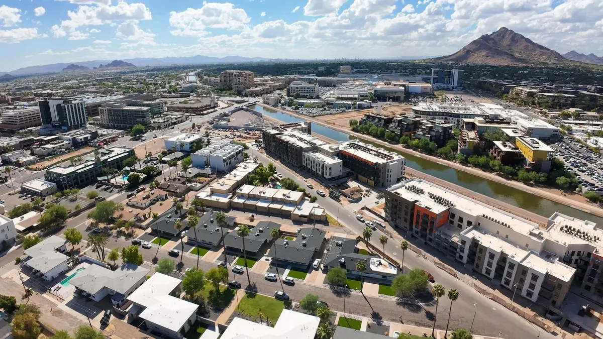 A wide-angle view of a river bordered by modern buildings, green spaces, and a mountainous backdrop. People can be imagined walking along the river, exploring urban areas, or dining at outdoor cafes, all of which contribute to an energetic, metropolitan atmosphere.