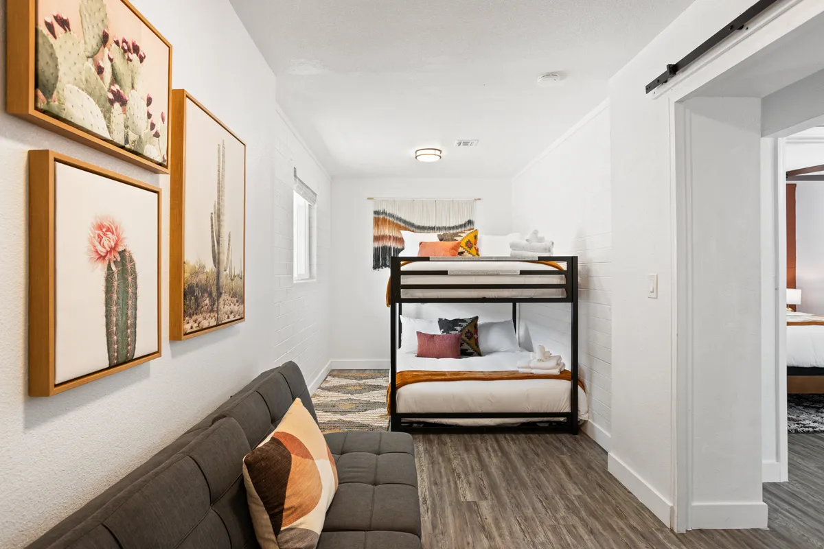A spacious bedroom designed for groups or families, featuring a sturdy bunk bed with two queen mattresses, a comfortable sofa for lounging, and framed artwork adding a playful, homey touch. The room exudes comfort and flexibility for family bonding and restful sleep.