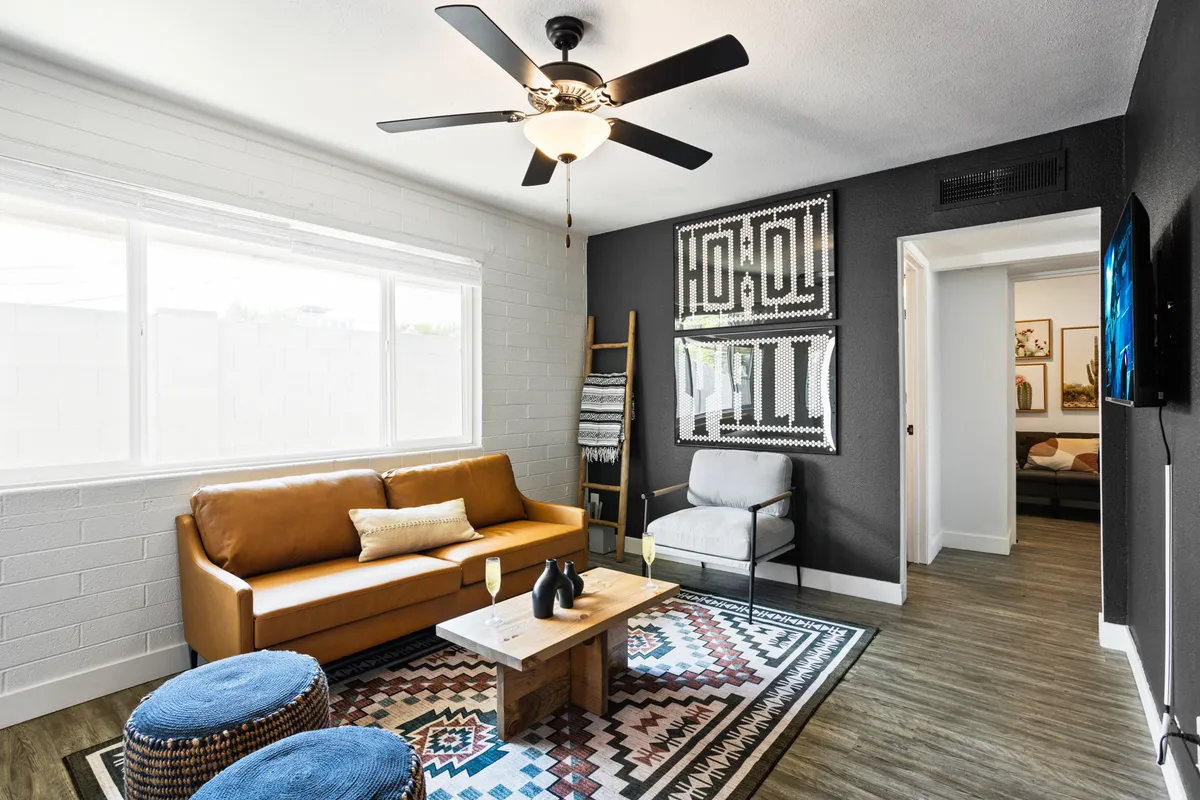 A cozy, modern living room featuring a leather sofa, stylish textured wall art, a colorful rug, and a wooden coffee table. The arrangement is designed for conversation and relaxation, creating a warm, modern lounge feel.
