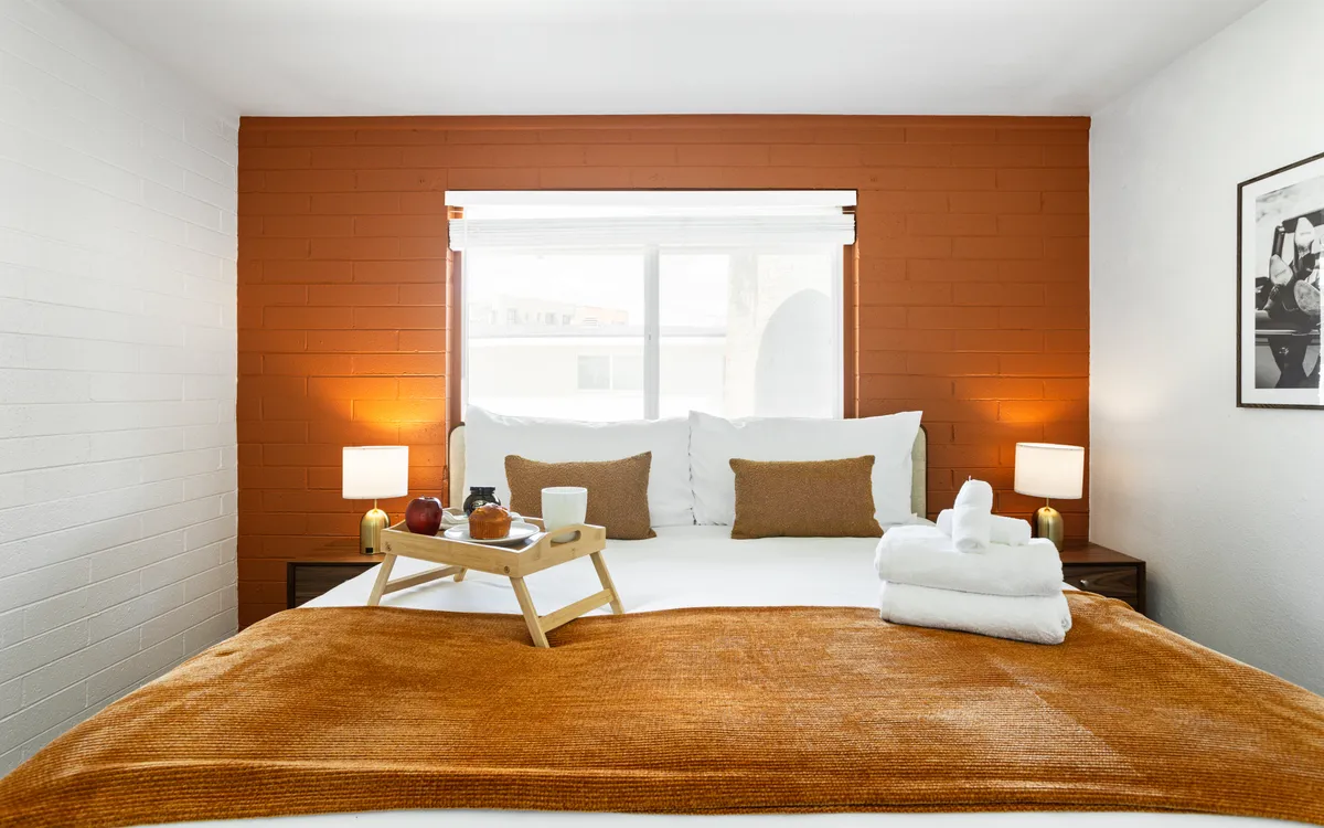 A cozy bedroom with a well-made bed, decorative pillows, a tray with breakfast items, dual nightstands, and a sunlit window. The room feels welcoming and intimate, encouraging relaxation and leisurely mornings.