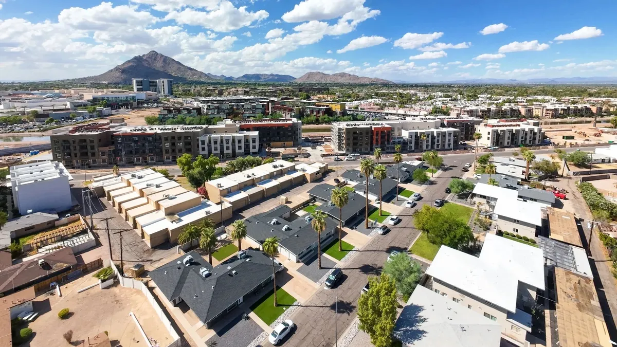 This photo captures residential buildings set against a dramatic mountain backdrop, punctuated by palm trees and nearby roadways. The image conveys a sense of community vibrancy, proximity to urban amenities, and the scenic beauty of the Scottsdale area.