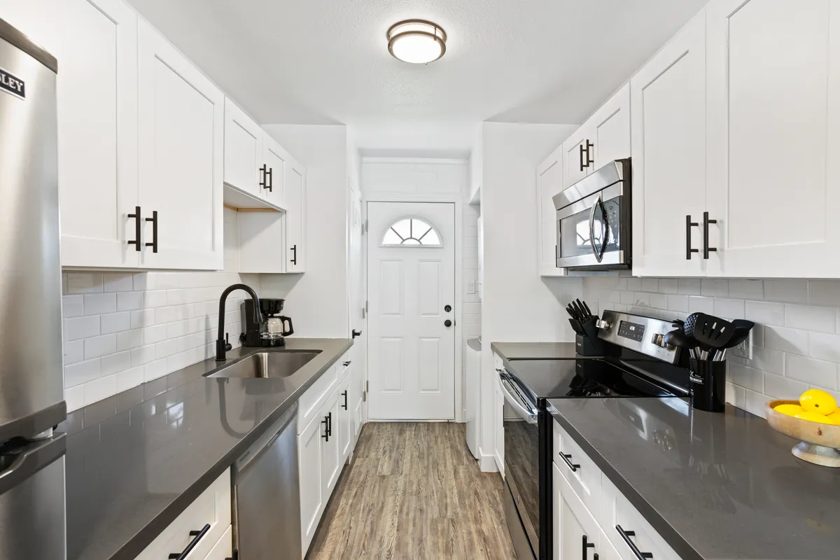 A sleek, modern kitchen featuring stainless steel appliances, gray countertops, and white cabinetry accented with black. The open counterspace is ideal for meal preparation or gathering, and the atmosphere feels both stylish and inviting. The scene suggests home cooking, baking, and socializing.