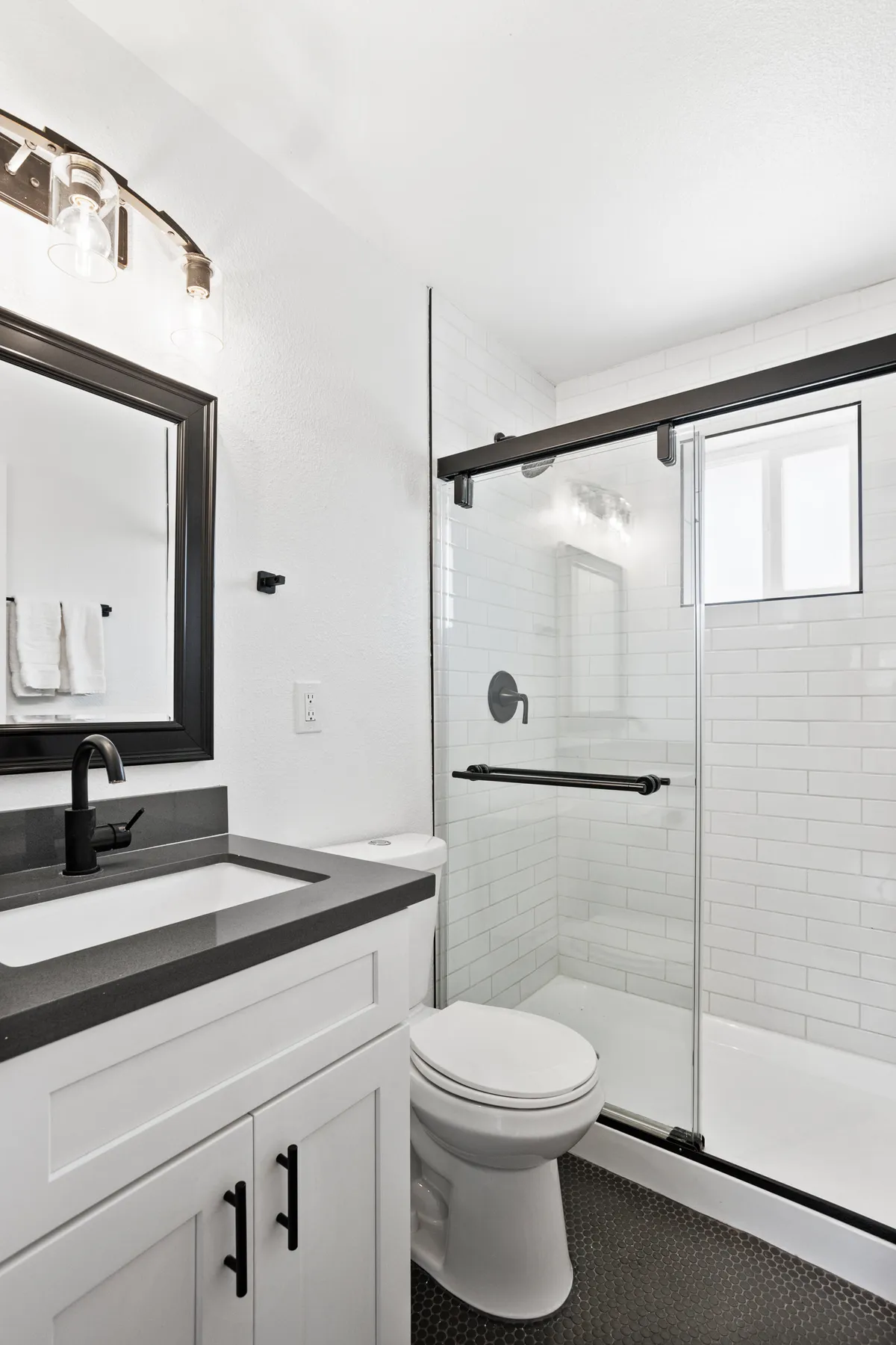 A modern, spa-inspired bathroom with a sleek vanity, glass shower enclosure, and black fixtures. The soft lighting and minimalist decor promote a sense of relaxation and rejuvenation, ideal for unwinding after a busy day.