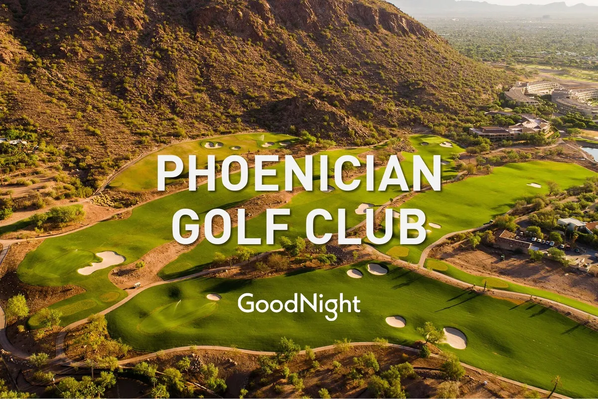 A panoramic view of a lush golf course with perfectly manicured green fairways, set against a dramatic mountain backdrop. The elegant clubhouse is visible, adding a touch of luxury to the scenic, natural landscape.